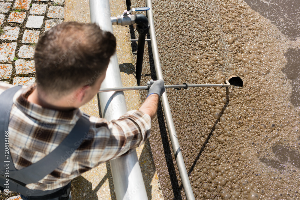 Worker taking water sample out of clarifier tank of sewage treatment plant