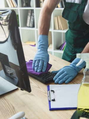 Cropped shot of professional cleaner in rubber gloves cleaning computer keyboard in office