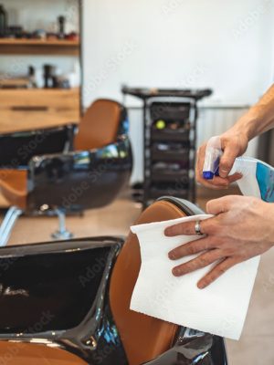 Hair stylist cleaning his work space during pandemic isolation, he wears protective equipment. Hair stylist disinfecting work space. Hair cutting during pandemic