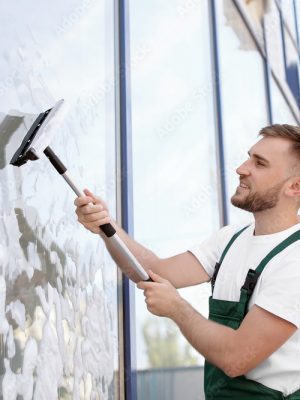 Male cleaner wiping window glass with squeegee from outside