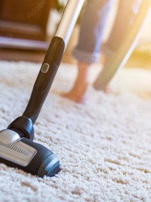 Woman using a vacuum cleaner while cleaning carpet in the house.